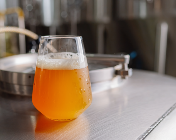 a close up photo of a stemless teku glass filled with NEIPA. the glass is on a flat tnk